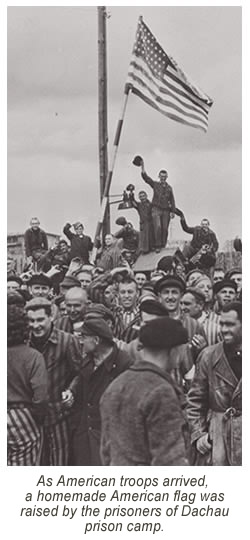 “As American troops arrived, a homemade American flag was raised by the prisoners of Dachau prison camp. As it waved in the breeze, it seemed to reflect the joy of inmates who realize freedom for the first time in many years.